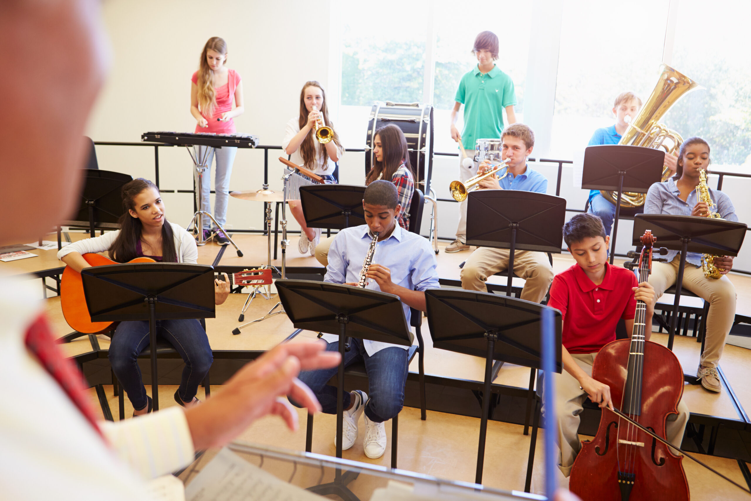 Pupils Playing Musical Instruments In School Orchestra With Tutor Conducting
